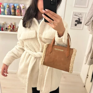 Vit teddyjacka med knytband - Mysig vit teddyjacka med knytband i midjan. Jackan har långa ärmar och en avslappnad passform, perfekt för kyligare dagar. Nypris 600kr