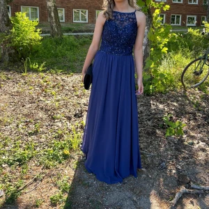 Mörkblå balklänning med paljetter på överdelen - Elegant mörkblå balklänninh med vackra paljettdetaljer och spetsmönster på överdelen. Superfin i solljuset! Använd fåtal gånger och omsydd är 157 och den va perfekt längd för mig när jag hade klackar.  Mått= midja-31 längd-137 byst-37.