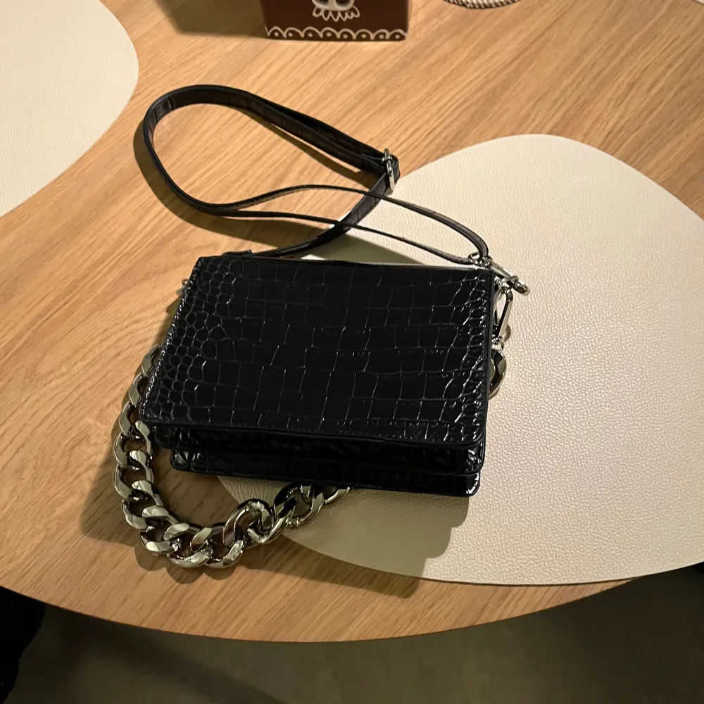 Svart axelväska från Bershka i krokodilmönstrat lackat fuskskinn med en silverfärgad kedja. Justerbar, avtagbar axelrem. Kedjan går att haka på/av. Stängs med magnetlås. Nyskick!! ✨. Laukut & Käsilaukut.
