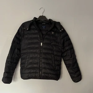 GANT jacka st 160 - Säljer en svart tun dunjacka från Gant med dragkedja och huva. Jacakn är i storlek 14 år och passar bäst 164-155cm. Skick 7/10 nå smuts som sitter fast i höger ficka men Inga hål eller annat bara lite sliten . Bara att skriva för eventuella frågor