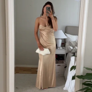 Guld/Champagnefärgad axelbandslös balklänning - Balklänning i guld/champagne färg från ASOS i storlek 38/M. Jag är en S i vanliga fall och den sitter bra på mig. Jag är även 170cm lång och den går i marken för mig.  Mått: Byst rakt över: 39cm Längd fram: 131cm Längd bak: 129cm