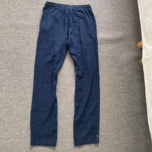 Mörkblå linnebyxor med snörning - Snygga mörkblå linnebyxor med rak passform och elastisk midja. Byxorna har praktiska fickor och en dekorativ snörning framtill med träpärlor. 