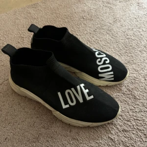 Moschino tyg skor strl 41  - Love Moschino skor i strl 41 i okej skick. Använda några år sedan. Slitmärke på ena skon, se sista bilden. Köpta för ca 1850kr.