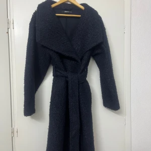 Svart teddyjacka med bälte - Säljer en mysig svart teddyjacka med bälte. Jackan har långa ärmar och en stor krage som ger en stilren look. Perfekt för kyliga dagar när du vill hålla dig varm och trendig.