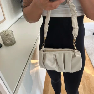 Beige axelväska med dragkedja - Snygg vit axelväska med dragkedja och veckad design. Perfekt för att bära med sig det nödvändigaste. Väskan har en stilren look. Aldrig använd 