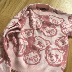 Rosa stickad tröja med björnmönster från Shein - Säljer en söt rosa stickad tröja från Shein med ett unikt björnmönster. Tröjan har långa ärmar och ribbade muddar vid ärmslut och hals. Perfekt för en mysig dag!