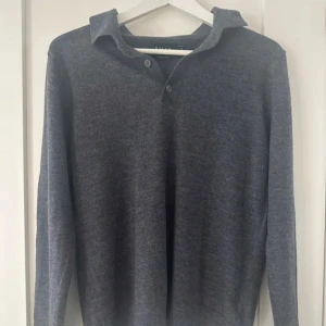 Merinoull tröja  - Säljer en stilren grå långärmad tröja med krage och knappar framtill. Perfekt för en avslappnad men ändå uppklädd look. 