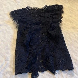 marinblå spetsblus från Zara - Säljer en elegant spetsblus från Zara. Blusen är ärmlös och har ett vackert blommönster i spets. Perfekt för att ge en sofistikerad touch till din outfit. Slutades sälja 2023. 