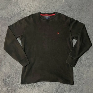 Ralph lauren tröja  - Säljer en stilren svart långärmad tröja från Polo Ralph Lauren med röd logga på bröstet. Tröjan har en klassisk rund halsringning och är perfekt för en avslappnad look. Passar bra till jeans eller chinos.