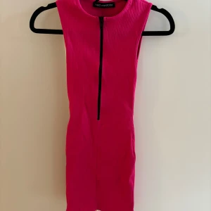 Rosa ribbad klänning från Naked Wardrobe - Snygg rosa ribbad klänning från Naked Wardrobe med dragkedja framtill. Den är ärmlös och har en tight passform som framhäver figuren. Perfekt för en kväll ute eller en speciell tillställning. 💖