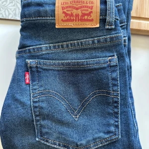 Levi's Ribcage Straight Ankle Jeans - Snygga Levi's Ribcage Straight Ankle jeans i klassisk blå denim. De har en hög midja och raka ben som ger en tidlös look. Perfekta för en avslappnad stil med en touch av vintagekänsla.