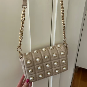 Beige axelväska med pärlor - Snygg beige väska med pärlor. Perfekt för att lyfta vilken outfit som helst!! Går att ta av axelremmen och använda väskan som clutch🤩