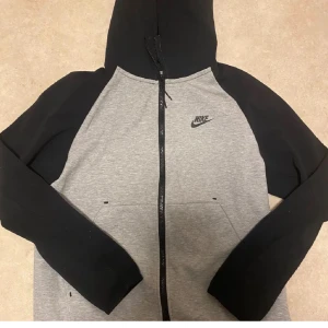 Nike tech (old season) passar både S/XS - (FRI FRAKT)           Säljer en snygg grå och svart hoodie från Nike med dragkedja framtill. Tröjan har en klassisk design med huva och långa ärmar. Perfekt för en avslappnad stil.                 (FRI FRAKT)