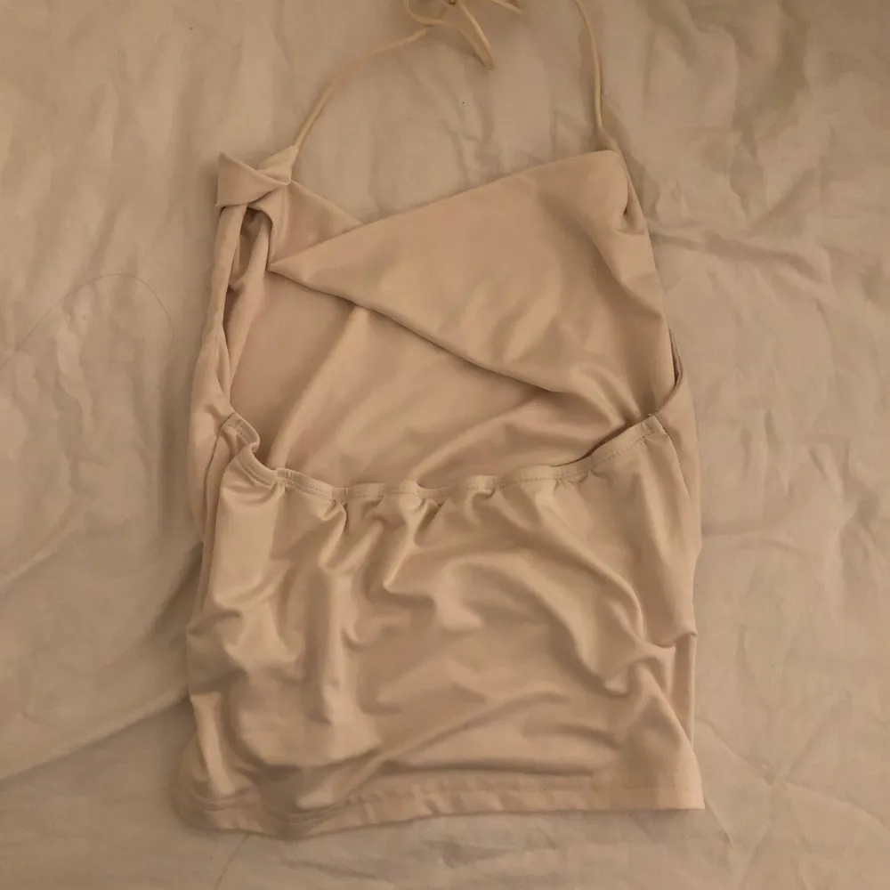 Säljer ett stilrent beige halterneck linne med draperad framsida. Perfekt för en somrig look. Linnet har tunna band som knyts i nacken. Jag vet inte storleken men det känns som ett S. Yläosat.
