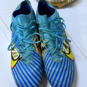 Blå randiga fotbollsskor från Nike elite - Snygga blå fotbollsskor från Nike med randigt mönster och gula detaljer. Skorna har snörning och en slitstark sula med dobbar för bra grepp på planen. Perfekta för fotbollsträning och matcher.