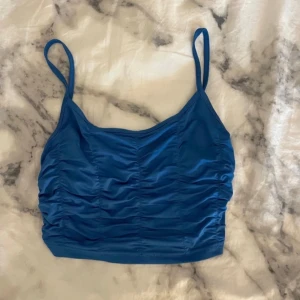 Blå linnetopp - Snygg blå linnetopp med smala axelband och rynkad detalj framtill. Perfekt för varma dagar eller som ett lager under en jacka. Enkel och stilren design som passar till mycket.