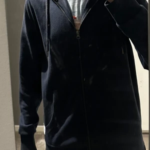 Mörkblå hoodie med dragkedja - Säljer en stilren mörkblå hoodie med dragkedja och långa ärmar från Jack & Jones. Knappt använd så den är i riktigt bra skick! Storlek S.