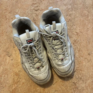 Vita sneakers från Fila - Säljer ett par vita Fila sneakers med snörning och märkets logga på sidan och baksidan. Skorna har en chunky sula. Skorna är lite fula inuti där hälen är, efter att jag haft skoskav i dem. Dem är i strl 42, men dem passar mig bra och själv har jag i vanliga fall 39-40. Priset kan absolut diskuteras! Du står för frakt😊