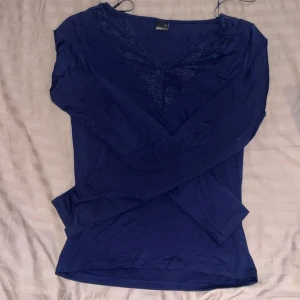 Mörkblå topp med spets från Gina Tricot - Supersnygg mörkblå långärmad topp från Gina Tricot med v-ringning och dekorativ spetsdetalj framtill. Tunn och mjuk i materialet, perfekt för lager-på-lager eller som den är. Sitter snyggt och har en feminin touch med spetsen.