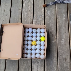  35 stycken blandade golf bollar i olika märken - Bilderna visar en kartong fylld med 35 stycken golfbollar av olika märken och skick, bland annat Titleist. Perfekt för dig som vill komma igång med golf eller behöver extra bollar till träningen. Passar både nybörjare och erfarna golfare som vill ha kul på banan.