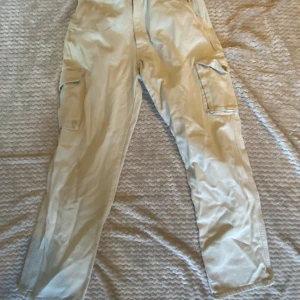 Beige cargobyxor från Versace Jeans - Snygga beige cargobyxor från Versace Jeans Signature med raka ben och stora fickor på sidorna. Byxorna har klassisk cargostil och är tillverkade i bomull för en skön känsla. Perfekta för dig som gillar streetwear med exklusiv touch.