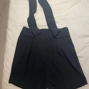 Mörkblå shorts med snören H&M - Snygga mörkblå shorts från H&M med breda snören och hög midja. Shortsen har fickor fram och bak samt en stilren design som ger en cool och trendig look. Perfekta för dig som vill sticka ut lite extra i sommar.