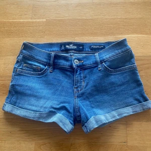 Blå lågmidjade low waist jeansshorts från Hollister - Snygga blå jeansshorts från Hollister med låg midja och uppvikta benslut. Klassisk femficksmodell med stretchigt material för extra komfort. Perfekta för varma sommardagar och har diskret Hollister-logga på bakfickan. Storleken är typ XS