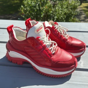 Röda chunky sneakers från Bronx - Snygga chunky sneakers från Bronx i rött och vitt med coola detaljer. Ovandelen är en mix av skinn, mocka och glansiga paneler. Tjock vit och röd sula, vita snören och logga på plösen. Perfekta för dig som vill sticka ut med färg och stil.