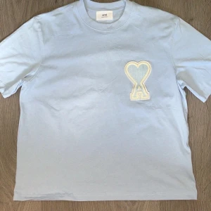 T-shirt Ami Paris - Snygg ljusblå t-shirt från Ami Paris med stort broderat hjärta och A-logga på bröstet. Den sitter som en M i längden men den är bred som en L. Ställ frågor vid funderingar 