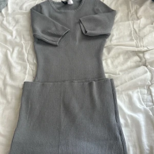 Grå ribbad kortklänning från Divided - Säljer en grå ribbad kortklänning från Divided. Klänningen har trekvartsärm, rund halsringning och är figurnära i modellen. Materialet är mjukt och stretchigt med en blandning av polyester, polyamid och viskos. Perfekt för en stilren och enkel look.