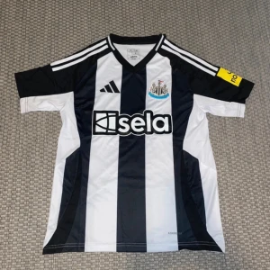 Newcastle United 24/25 matchtröja SMALL - Snygg Newcastle United fotbollströja från 24/25 säsongen HEMMA i Small storlek. Klassisk svartvit randig design med klubbmärke på bröstet och sponsortryck. Tillverkad i lätt och ventilerande Aeroready-material, perfekt för match eller träning.