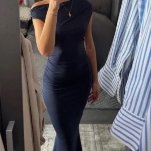 Marinblå långklänning offshoulder - Säljer en elegant marinblå långklänning med offshoulder-design och figurnära passform. Klänningen har en stilren och enkel look som framhäver siluetten. Perfekt för dig som vill ha en klassisk och tidlös stil.