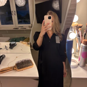 Svart skjortklänning - Svart skjortklänning med trekvartsärmar och puffiga axlar. Klänningen har knappar framtill och en rak, lite loose passform som slutar strax ovanför knäna. Perfekt för dig som gillar stilrena och enkla plagg.