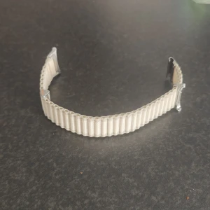 Vitt orginal Samsung watch ultra klockarmband - Snyggt vitt klockarmband från Samsung med tydligt randigt mönster. Tillverkat i textilmaterial med silvriga metalldetaljer. Perfekt för dig som vill ge din smartwatch en clean och stilren look.