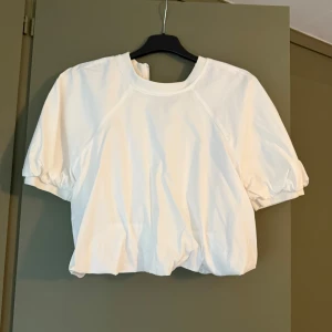 Vit croppad blus med puffärm - Superfin vit blus med korta puffärmar och croppad passform. Rund halsringning och resår i ärmslut och nederkant, ger en cool ballongeffekt. Perfekt i sommar med en kjol eller raka jeans. Använd en gång 