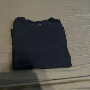 Svart t-shirt från Hugo Boss - En stilren svart t-shirt från Hugo Boss med diskret broderad logga på bröstet. Klassisk rund halsringning och korta ärmar. Perfekt basic-plagg i mjuk bomull som funkar till allt. Snygg och enkel design för en clean look. Hör av er vid minsta lilla fråga 