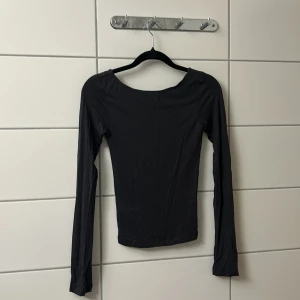 Svart långärmad topp med öppen rygg - Säljer en svart långärmad topp med tight passform och djup, öppen rygg. Toppen har en enkel och stilren design med rundad halsringning framtill och är tillverkad i ett stretchigt material som sitter snyggt på kroppen. Perfekt för dig som gillar minimalistisk stil.