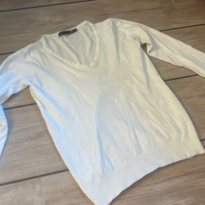 Vit v-ringad tröja från lager 157, XS - Klassisk vit v-ringad tröja från lager 157 i storlek XS. Tröjan har lång ärm och ribbade muddar vid ärmslut och nederkant. Enkel och stilren modell som passar perfekt till jeans eller kjol. 