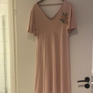 Ljusrosa vadlång från Cream, - Superfin ljusrosa långklänning från Cream med v-ringning både fram och bak, korta vida ärmar och broderad blomdetalj på bröstet. Mjuk och skön i bomull, perfekt för sommarens alla tillfällen. Sitter snyggt och har en flowy känsla.