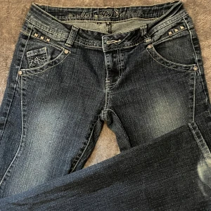 Miss Hot jeans med nitar och strass - Mörkblå jeans från Miss Hot med snygga slitningar, dekorerade med silvriga nitar och strassdetaljer på fickorna både fram och bak. Low-waist och utsvängda! Mått: midja: 34 cm (tvärsöver). Innerbenslängd: 80 cm🥰🥰