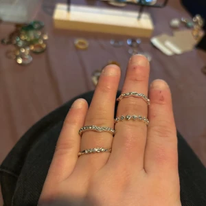 Set med fyra silvriga ringar med stenar - Fyra tunna silvriga ringar med glittrande stenar runt hela bandet. Några av ringarna har vågig form och andra är raka, vilket ger en snygg mixad look. Perfekta att bära tillsammans eller var för sig för en trendig vibe.