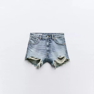 Blå jeansshorts med slitningar från Zara - Snygga blå jeansshorts från Zara med hög midja och råa, slitna kanter. Klassisk femficksmodell i denim med fransiga benslut och slitningar framtill för en cool, avslappnad vibe. Perfekta för sommardagar och festivaler.