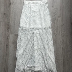 Vit spetskjol från Vero Moda - Supersöt långkjol från Vero Moda i vit spets med elastisk midja. Kjolen har ett genombrutet spetslager över ett helvitt foder som slutar ovanför knäna, vilket ger en snygg transparent effekt nedtill. Kjolen är lite tajtare,alltså inte så utsvängd vilket är rätt fin.Kjolen har använts en gång och är i mycket mycket bra skick.