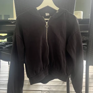 Svart hoodie med dragkedja från Lindex - Svart hoodie från Lindex med hel dragkedja och huva. Tröjan har långa ärmar, breda muddar i midja och ärmslut samt en enkel, clean look. Perfekt för chill dagar eller när du vill ha en basic stil. Materialet är mjuk bomullsmix.