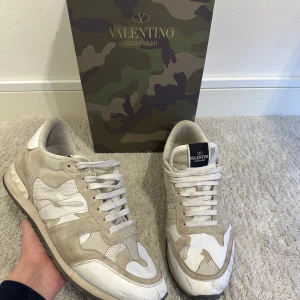 Valentino Garavani Rockrunner sneakers - Snygga Valentino Garavani Rockrunner sneakers i beige och vitt med coolt kamouflagemönster. Skorna har detaljer i mocka, mesh och skinn samt klassisk snörning. Ikoniska nitar på hälen och robust sula ger en exklusiv vibe. Perfekta för dig som gillar Old money med lyxig touch.