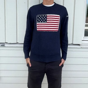 North Sails tröja - Snygg mörkblå stickad tröja från North Sails med amerikansk flagga broderad på bröstet och logga på ärmen. Tröjan har rund halsringning, ribbade muddar och är långärmad. Perfekt för dig som gillar klassisk och sportig stil.