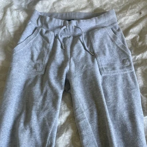 Grå mjukisbyxor Juicy Couture XS - Grå mjukisbyxor från Juicy Couture med snörning i midjan och stora fickor både fram och bak. Byxorna har silverfärgade knappar med logga på bakfickorna och är gjorda i mjukt bomullsmaterial. köpte dom för 1200kr och är använda cirka 3 gånger så jag väljer då att sälja dom för 900kr. skriv om de är nått ni undrar över😀