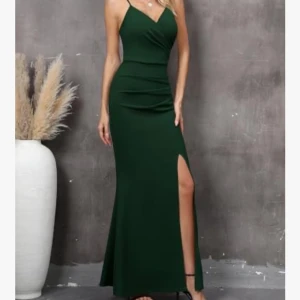 Mörkgrön långklänning med slits - Supersnygg mörkgrön långklänning med smala axelband och v-ringad omlott-topp. Klänningen har en figurnära passform upptill och en hög slits framtill som ger en extra cool touch. Perfekt för dig som vill sticka ut med en elegant och stilren look. Klänningen är oanvänd och har prislapp kvar.