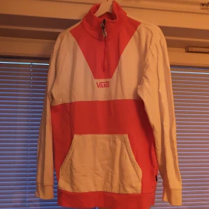 Vans rosa och vit half zip hoodie - Säljer en snygg hoodie från Vans i rosa och vitt med half zip och hög krage. Tröjan har en stor magficka ochVans-tryck på bröstet.. Långärmad och med relaxed passform.