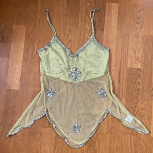 Grön mesh topp med paljetter Saint Tropez - Superfin ljusgrön linnetopp från Saint Tropez med tunna axelband och transparent mesh nedtill. Toppen har silvriga paljettdetaljer, broderade blommor och glittriga kanter. Oregelbunden nederkant ger en sagolik vibe. Perfekt för dig som vill sticka ut!